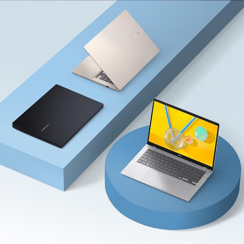 Three ASUS Vivobooks are placed on purple geometiric shapes. The platinum gold model is slightly open, the black model is closed, and the silver model is open.